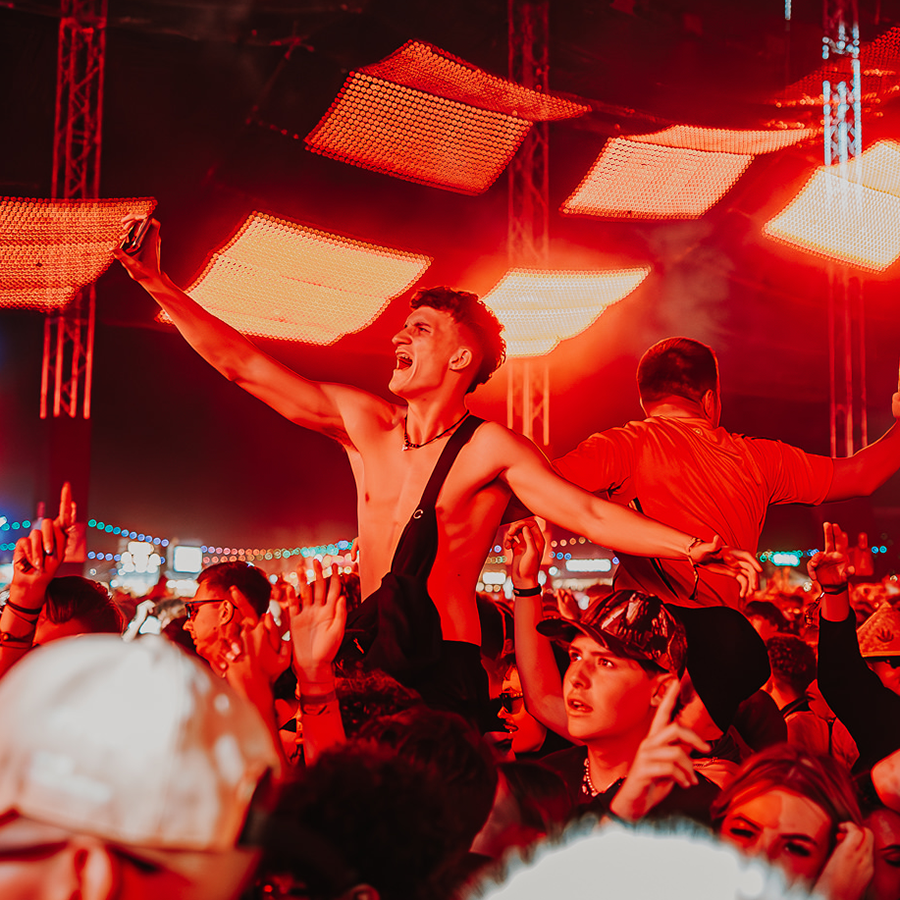 customer sitting on their friends shoulders under the orange lights of chevron stage at Reading Festival 