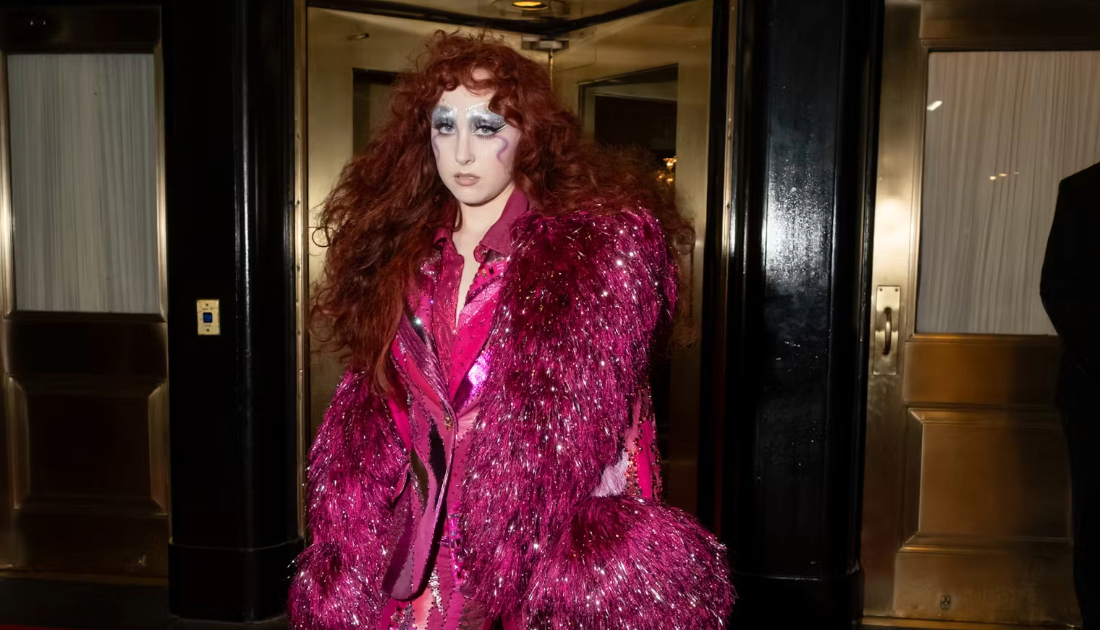 Chappell Roan wearing a two piece sequin lined suit in the colour hot pink at the met gala 2025, she has bright red auburn hair in big curls 