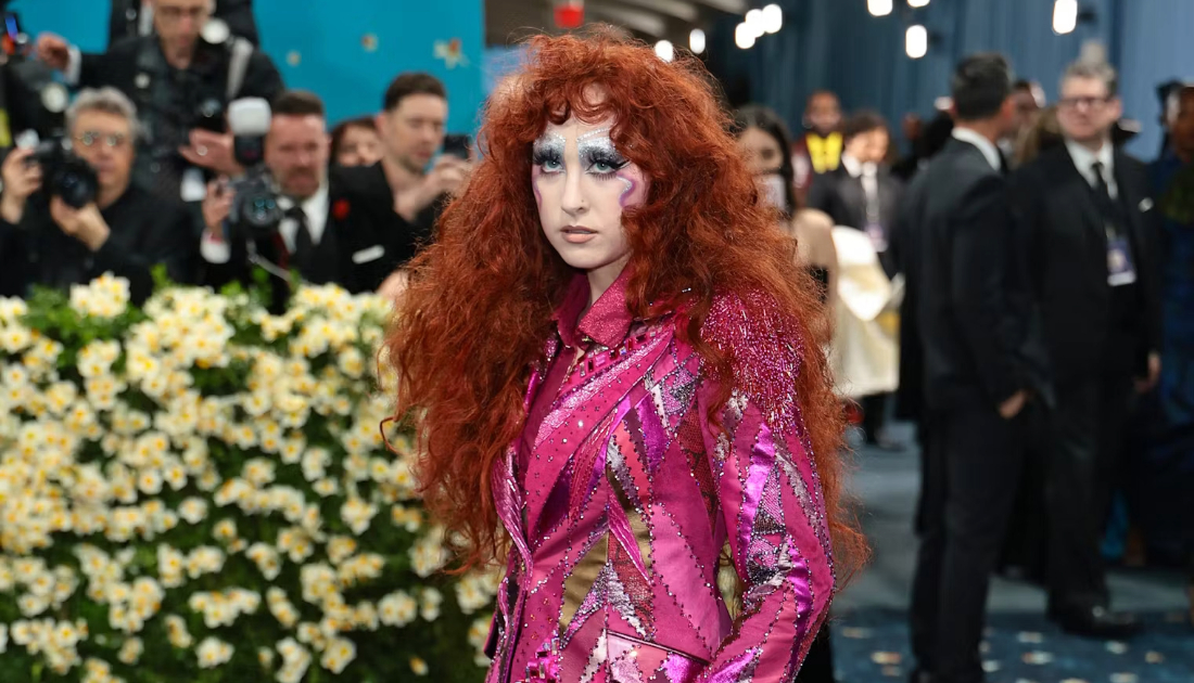 Chappell Roan wearing a two piece sequin lined suit in the colour hot pink at the met gala 2025, she has bright red auburn hair in big curls 