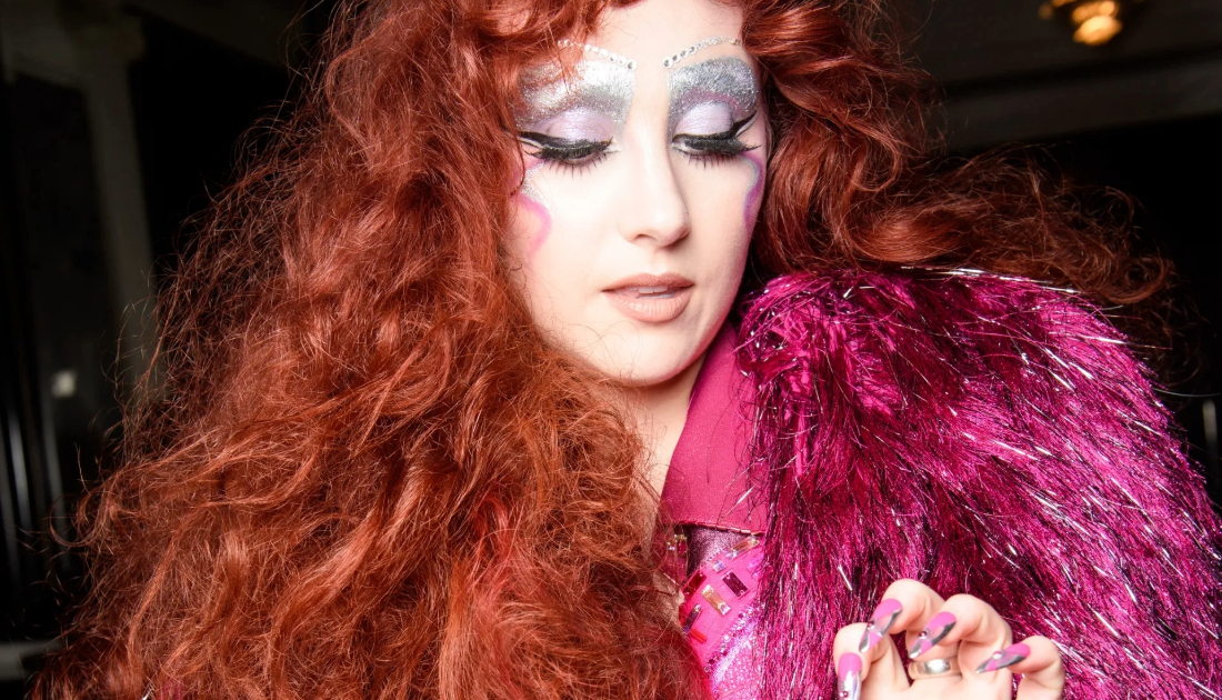 Chappell Roan wearing a two piece sequin lined suit in the colour hot pink at the met gala 2025, she has bright red auburn hair in big curls 